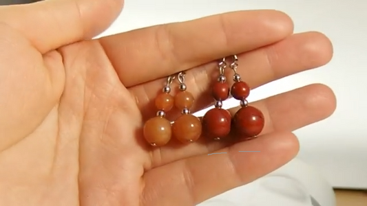 Hand holding a pair of red bead earrings with a blurred background